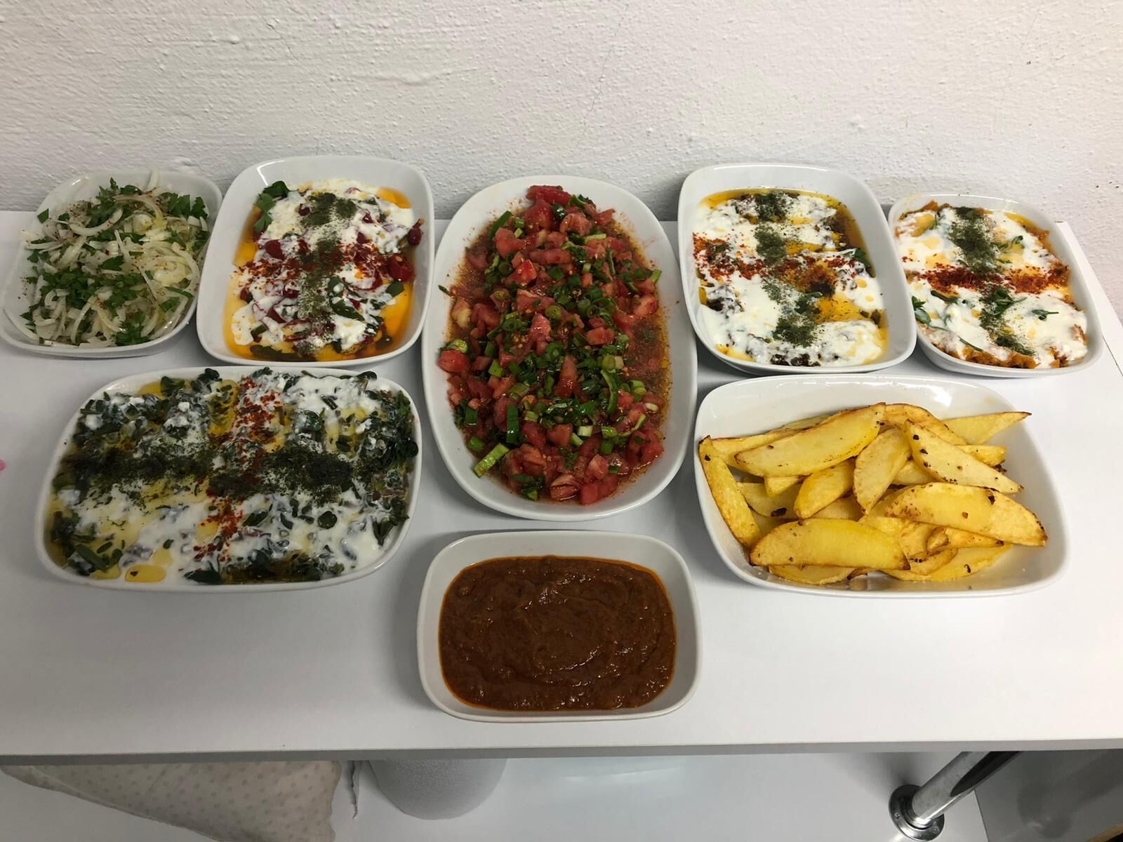 A table with various dishes including salads, a tomato-based dish, a potato dish, and a bowl of sauce.