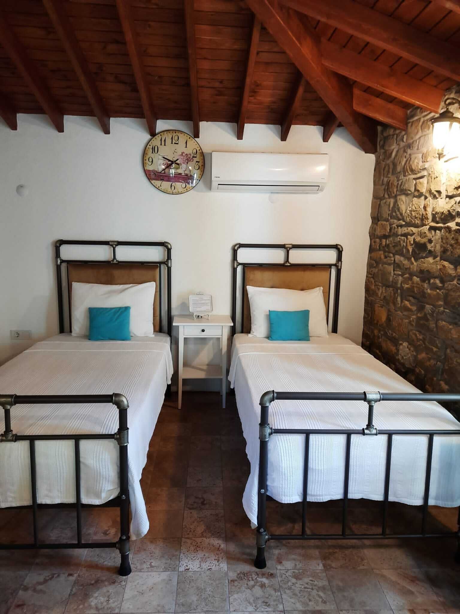 Una habitación con dos camas, techo de madera, pared de piedra y un reloj de pared.