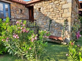 Una casa de piedra con un pequeño porche y un jardín lleno de flores rosas.