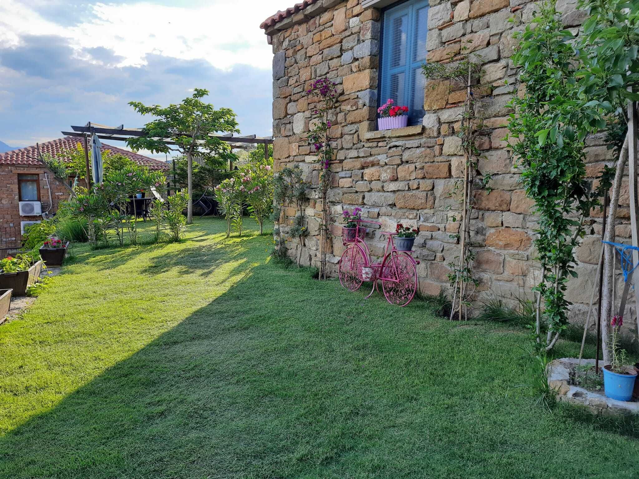 Un edificio de piedra con ventana y balcón, rodeado de un jardín cuidado con césped y plantas en macetas.