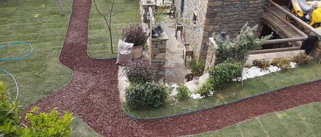 A stone building with a garden area featuring a lawn, mulch, and potted plants.