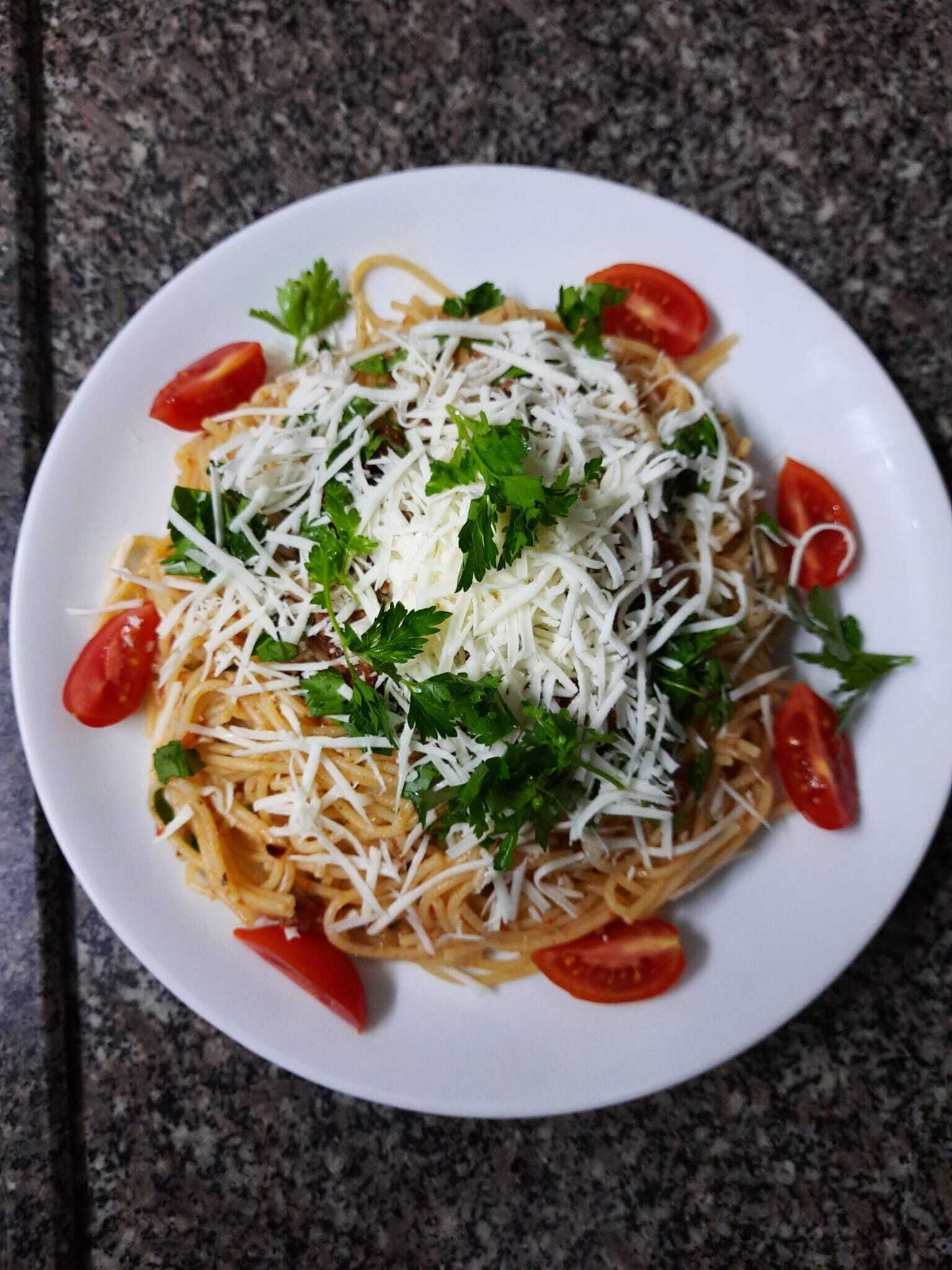 A plate of spaghetti with tomato sauce, topped with grated cheese and garnished with parsley and cherry tomatoes.