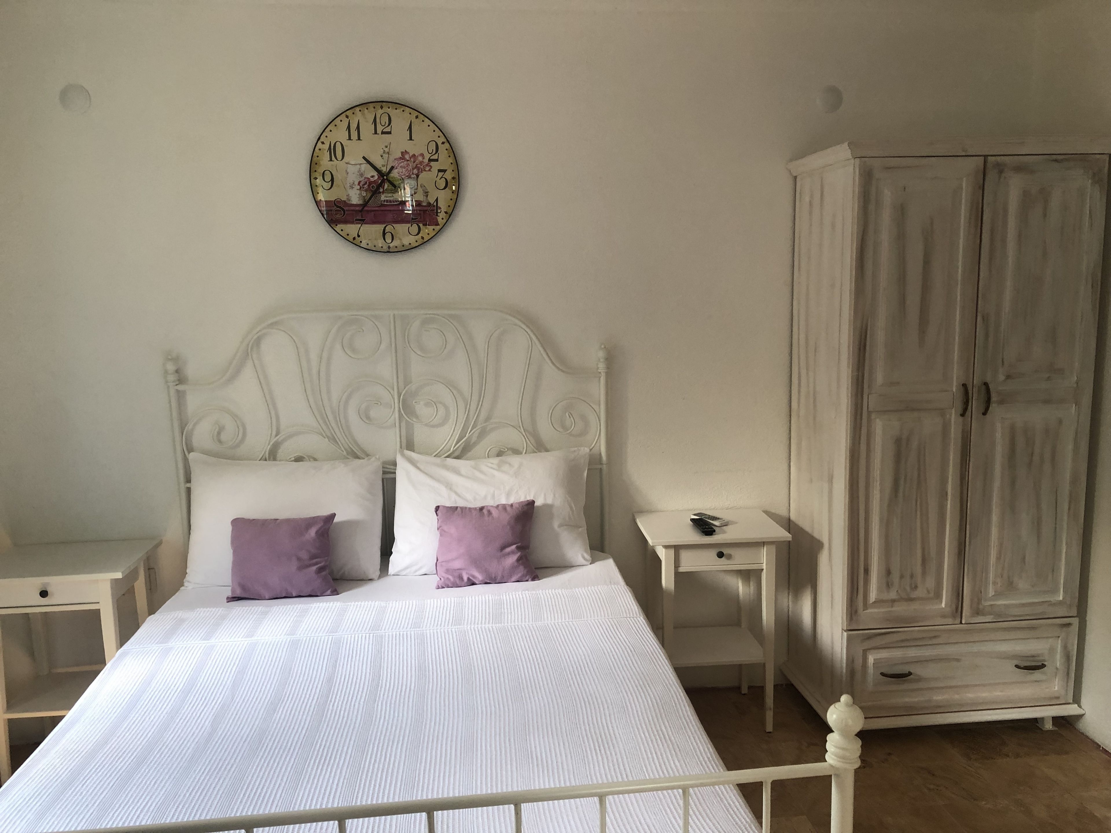 A bedroom with a white bed, two nightstands, a white wardrobe, and a wall clock.