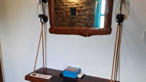 Une balançoire en bois rustique suspendue à un mur de pierre, un banc bleu avec coussin en dessous, et une petite table avec une boîte et une télécommande.