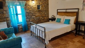 Une chambre avec un mur en pierre, un lit doté d’une tête de lit en bois, une table de chevet, une chaise bleue et une fenêtre avec des rideaux.
