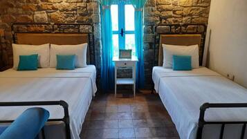 A room with two beds, a small table, and stone walls.
