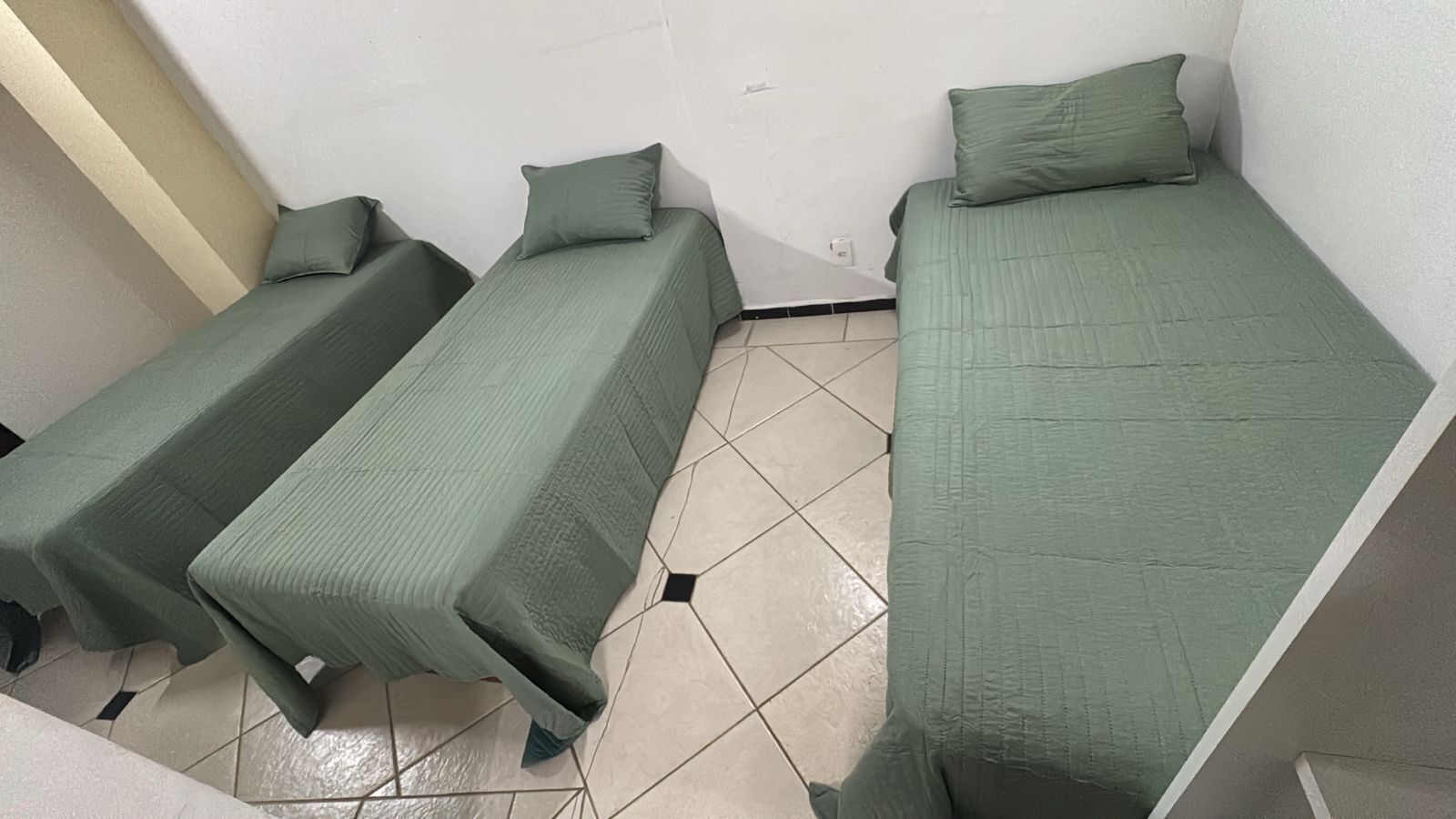 Three single beds with green bedding in a room with tiled flooring.