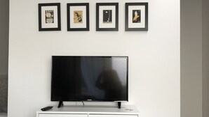 A white entertainment unit with a flat-screen TV, four framed artworks, and wooden legs.