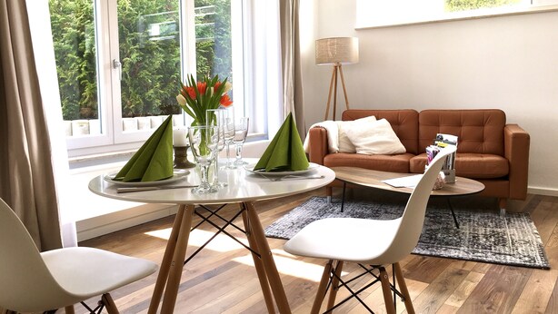 A modern living room with a dining table set for two, a sofa, and a floor lamp.