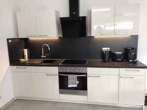 A modern kitchen with white cabinets, a black countertop, a stainless steel sink, a built-in oven, and a coffee maker. - Stylish and bike-friendly vacation apartment in Weimar (Oberweimar)