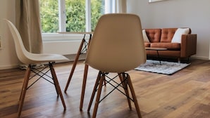 A modern living room with a wooden floor, a brown sofa, and two white chairs.