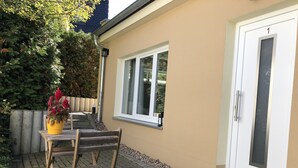 A patio with a wooden table and chairs, a yellow flower pot, and a white door with a number 1 sign.