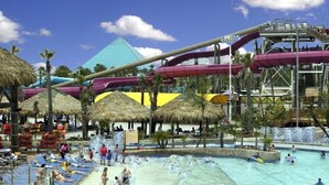 Un parque acuático con una piscina grande, toboganes de agua y sombrillas de paja.