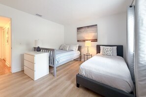 Une chambre à coucher avec un lit, un bureau et une chaise. Il y a un tableau au mur et une lampe sur le bureau.