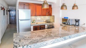 Uma cozinha moderna com bancadas de granito, eletrodomésticos de aço inoxidável, armários de madeira e iluminação pendente.