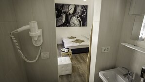 A modern hotel room with a bed, a small table with a cup and a book, a white telephone, and a bathroom with a sink and mirror. - Boutique accommodation Shappy (Zagreb)