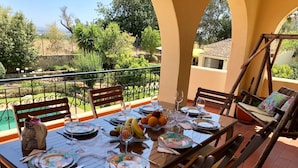 A dining table set for four on an outdoor patio with a view of the landscape. - Casa das Rosas, a peaceful stress-free villa to relax (Santa Bárbara de Nexe)