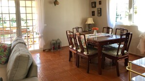 A dining area with a wooden table and chairs, a decorative lamp, and a view through a glass door to an outdoor patio. - Casa das Rosas, a peaceful stress-free villa to relax (Santa Bárbara de Nexe)