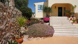 A stone wall, a flower bed, and a staircase leading to a building entrance. - Casa das Rosas, a peaceful stress-free villa to relax (Santa Bárbara de Nexe)