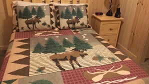 A bedroom with a wooden headboard, two decorative pillows with a forest theme, a nightstand with a lamp, and a digital clock displaying 1:37.
