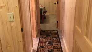 A wooden hallway with a patterned rug leading to a bedroom.