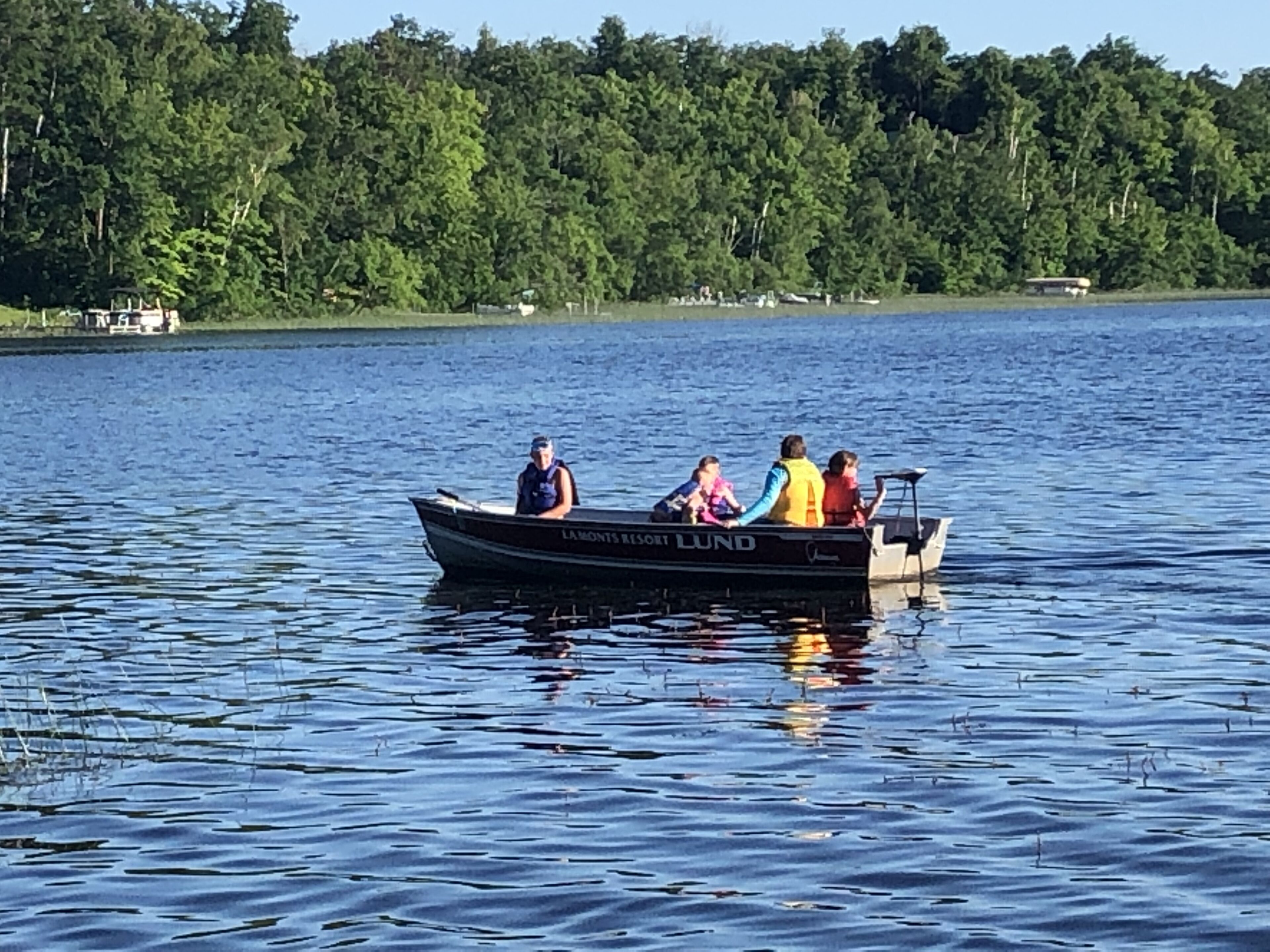 A boat with four people on a lake surrounded by trees.