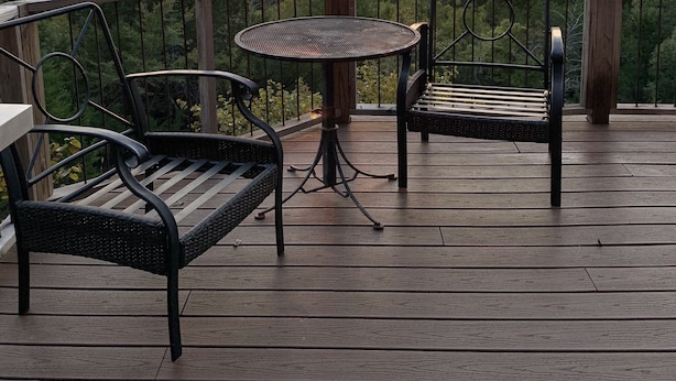 A wooden deck with a table and two chairs, overlooking a forested area and a body of water during sunset.