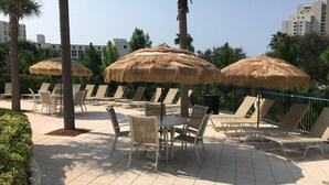 Un área de lounge en la azotea con sombrillas de paja, sillones reclinables y suelo de baldosas.