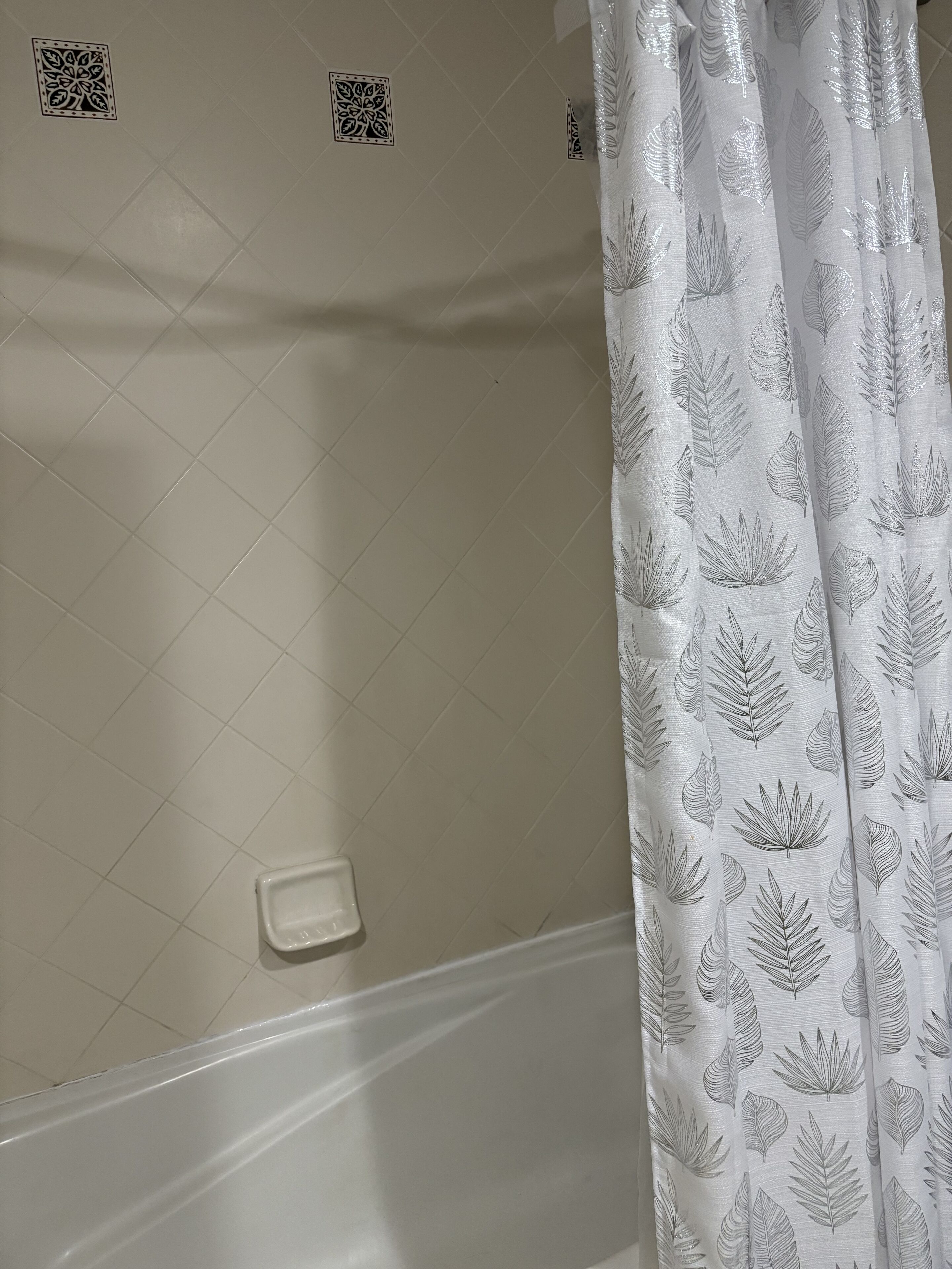 A bathroom with a white bathtub, a shower curtain with a leaf pattern, and a small soap dish on the wall.