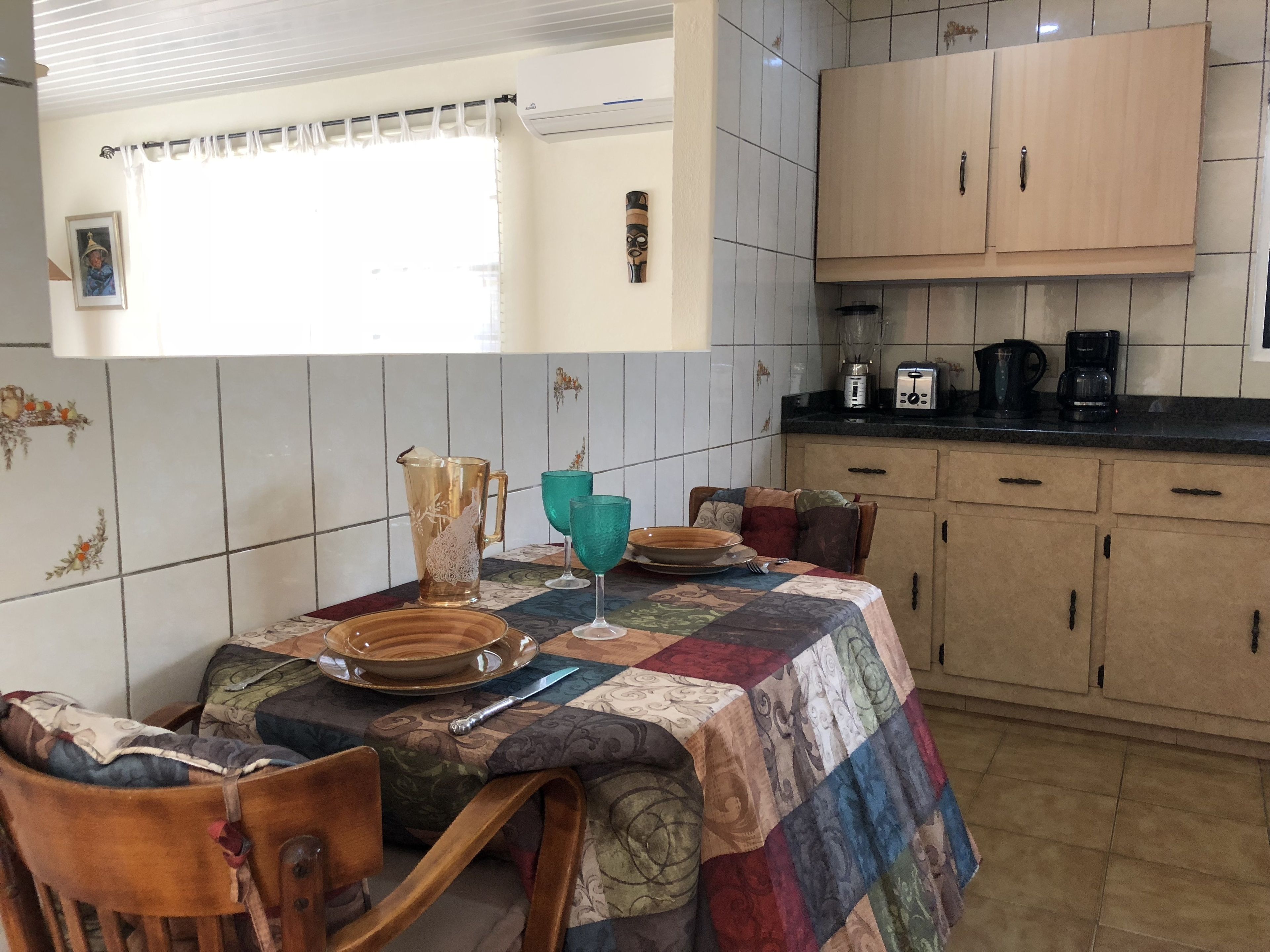 A kitchen with a dining table set for two, a coffee maker, and a blender on the counter.