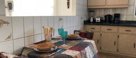 A kitchen with a dining table set for two, a coffee maker, and a blender on the counter.
