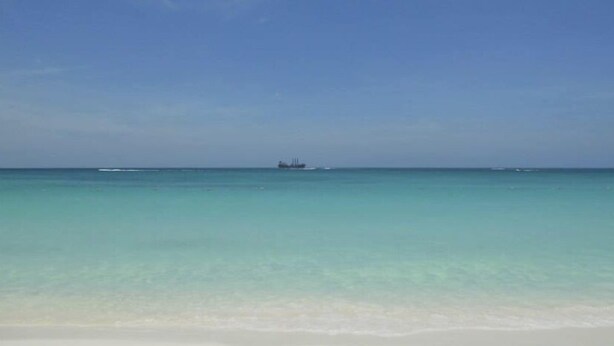 Una playa con agua turquesa cristalina y un barco a lo lejos.