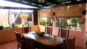 An outdoor dining area with a wooden table and chairs, surrounded by potted plants and a bamboo screen. - Caribbean Cozy Cove (Paradera)