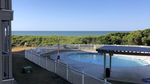 Ein Poolbereich mit weißem Zaun, einer überdachten Sitzgelegenheit und Blick auf das Meer.