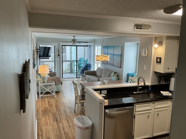 A modern kitchen with a black countertop, white cabinets, and a view to a balcony with outdoor furniture. - Dunescape with 3 ensuite full bathrooms. Private beach access chairs included! (Atlantic Beach)