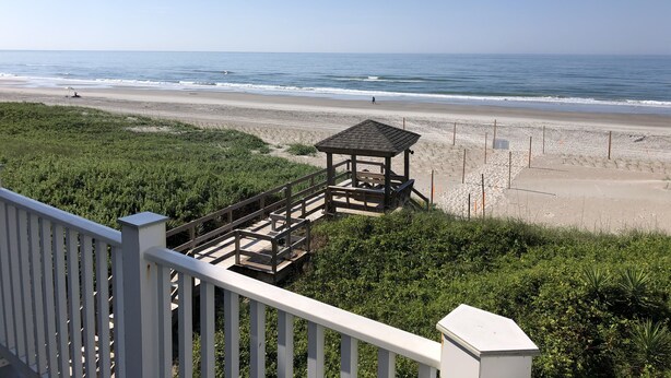 Blick auf einen Strand mit einem hölzernen Pavillon und einem weißen Geländer.