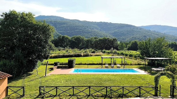 A pool with a pergola and lounge chairs, surrounded by a well-maintained lawn and a view of mountains.