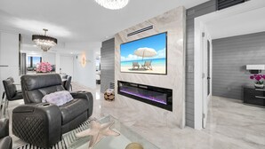 Ein modernes Wohnzimmer mit einer Ledersofa, einem Glastisch, einer Meeressterne-Dekoration, einem Kamin und einem großen Fernseher, der eine Strandansicht zeigt.