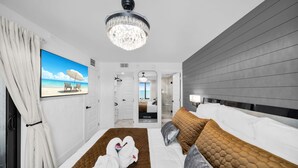 Ein modernes Hotelzimmer mit einem großen Bett, einem Kronleuchter, einem Strandbild und Meerblick durch das Fenster.
