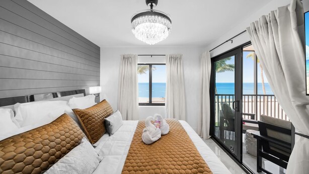 Ein modernes Hotelzimmer mit einem großen Bett, einer Kristallleuchter, einem Balkon mit Meerblick und einer Schiebeglastür.