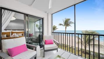 Een balkon met uitzicht op het strand, een bank met een roze kussen en een tafel met dienblad.