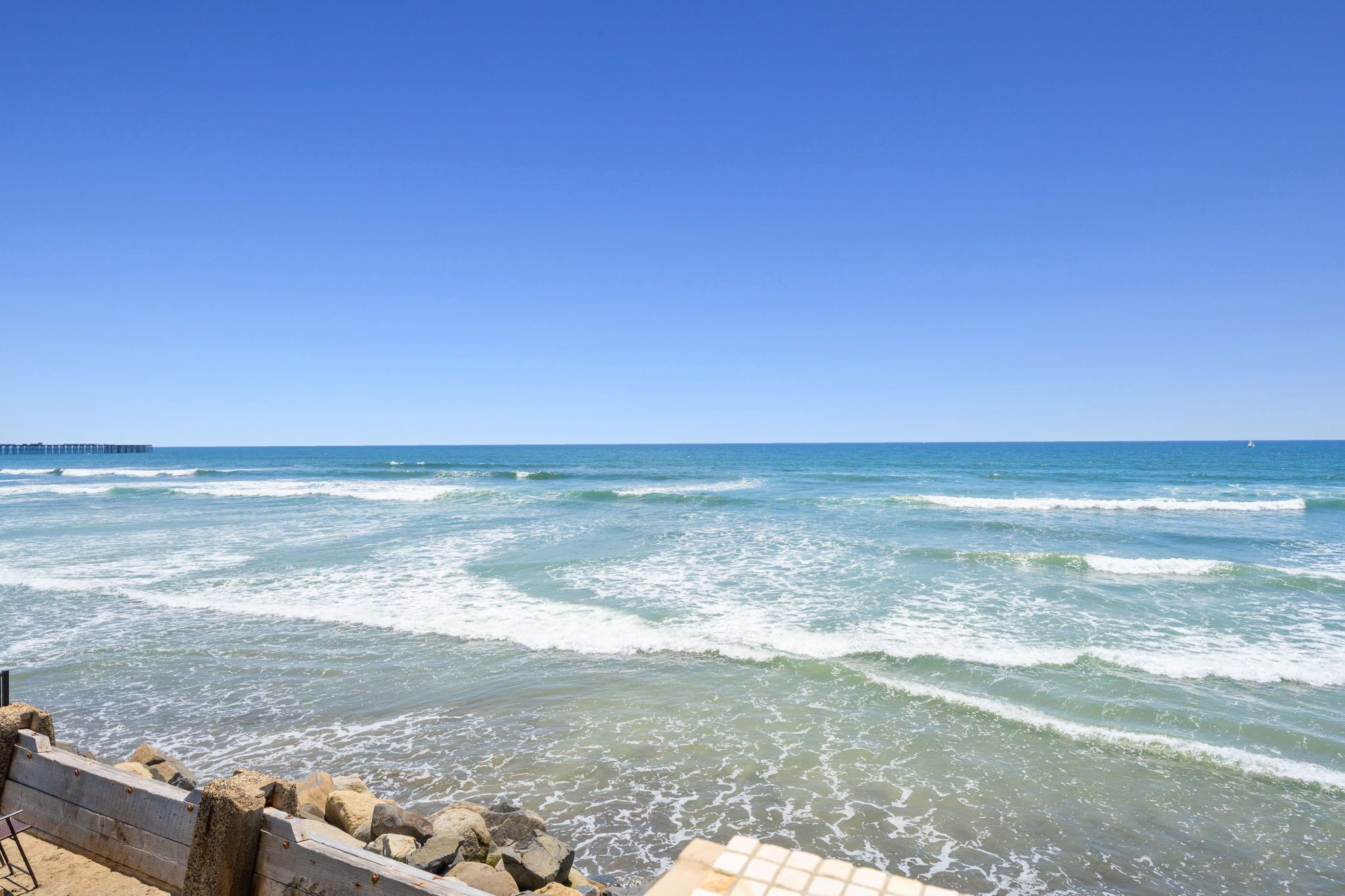 Vista sulla costa con onde, un molo e un litorale roccioso.
