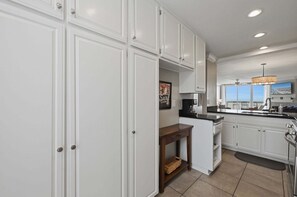 Une cuisine moderne avec des meubles blancs, une machine à café et une vue sur la ville grâce à de grandes fenêtres.