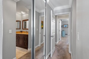 Un couloir avec une salle de bain comprenant un meuble-lavabo, une porte donnant sur une autre pièce et un sol recouvert de moquette.