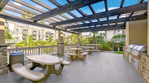 Une terrasse extérieure avec des tables et des bancs en pierre, un barbecue et une vue sur des immeubles résidentiels.