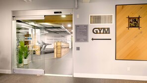 Der Eingang zu einem Fitnessstudio mit Laufband, Hinweisschild zu den Regeln und einem Pfeil, der den Weg weist.