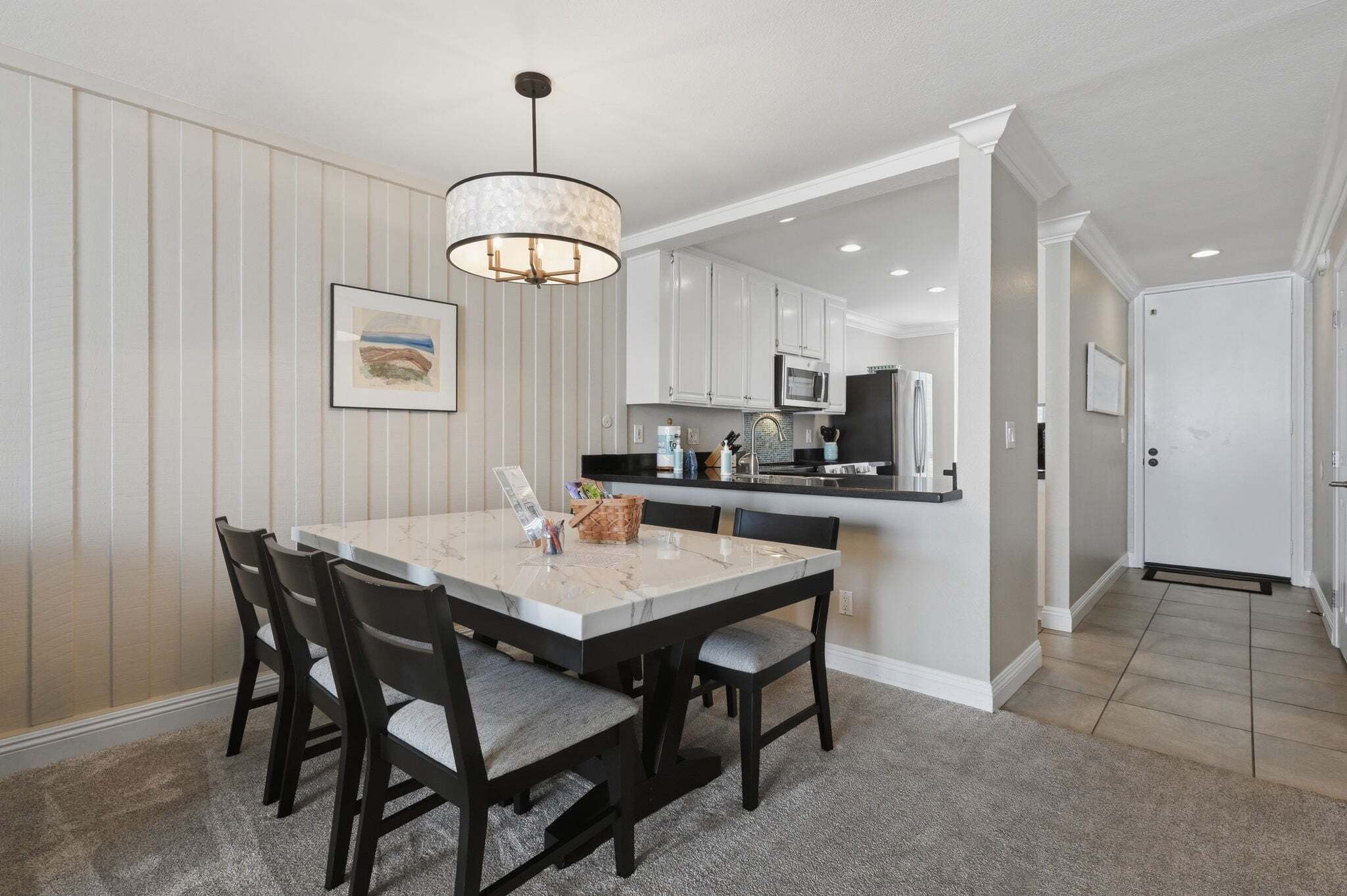 A dining area with a marble table and chairs, a pendant light, and a kitchen in the background.