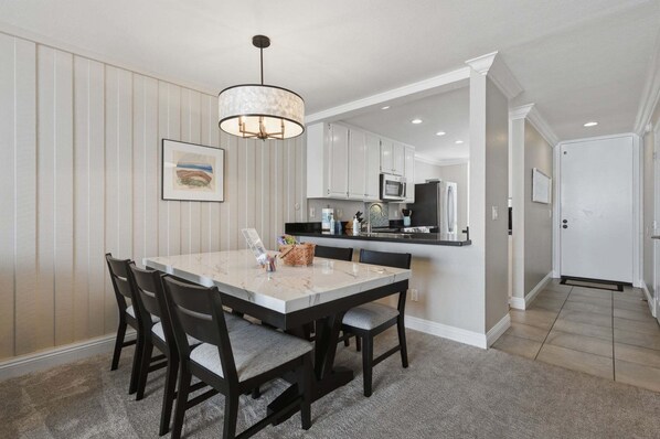 A dining area with a marble table and chairs, a pendant light, and a kitchen in the background.