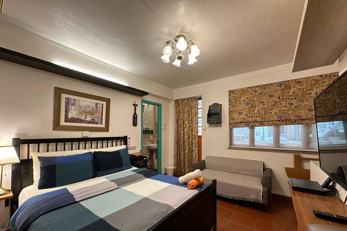 Un dormitorio con cama, un escritorio, una silla, una ventana con cortinas, una lámpara de techo y una estantería en la pared.