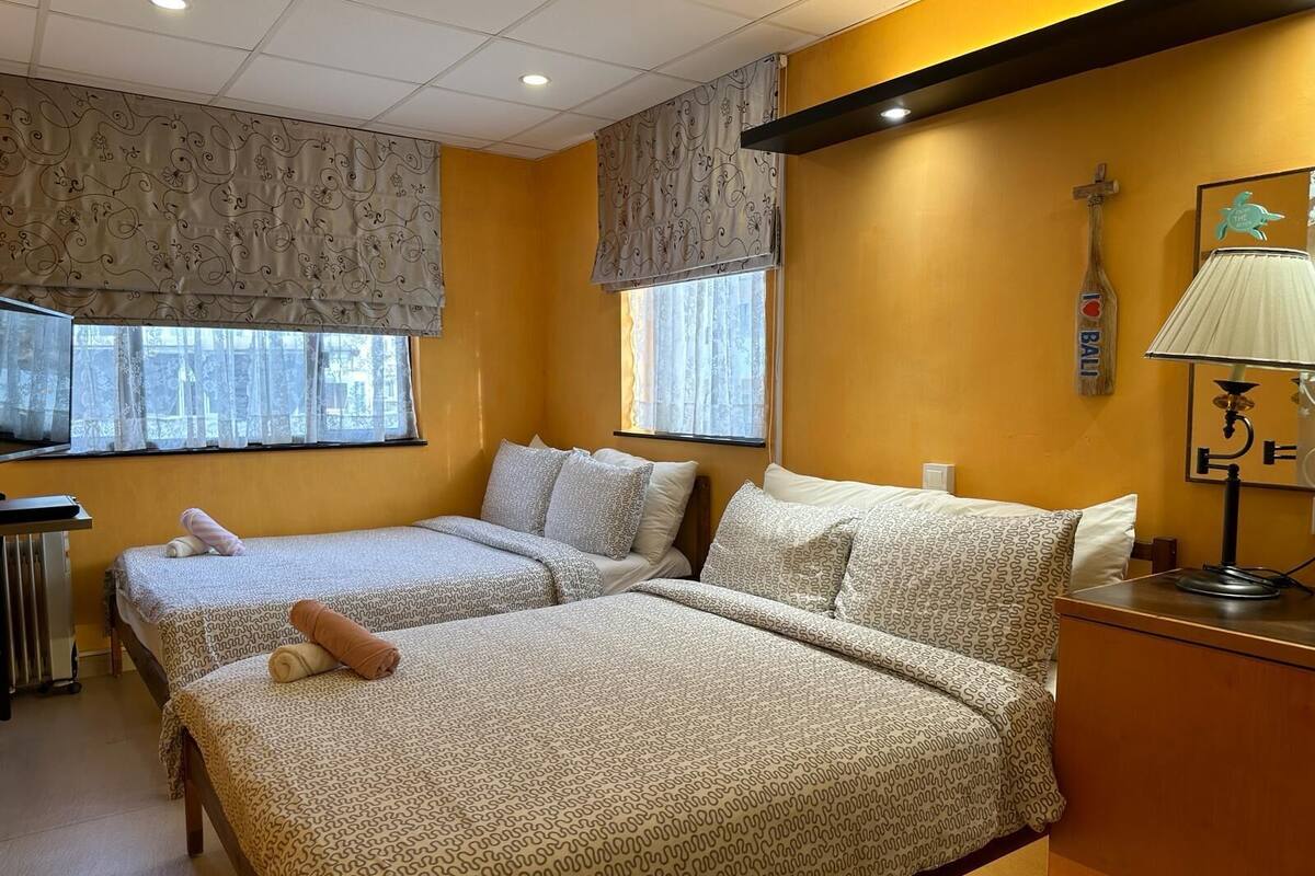 Habitación de hotel con dos camas, un escritorio, una lámpara y una ventana con cortinas.